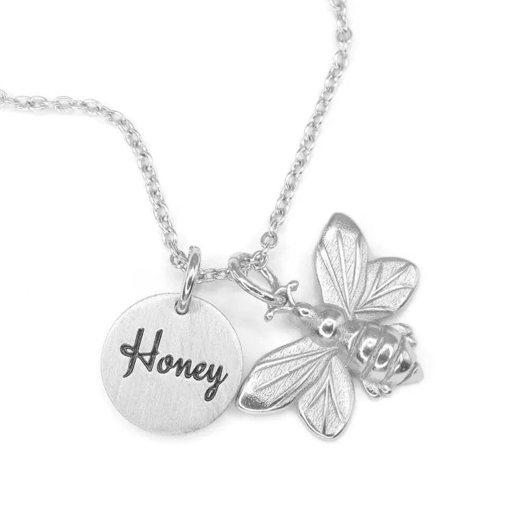 A silver necklace with a 3D honey bee charm, and a circular charm with the word Honey in a script font